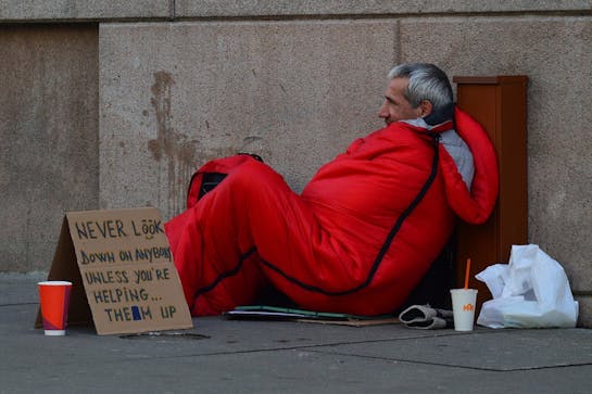 Person sleeping on street with sleeping bag and sign